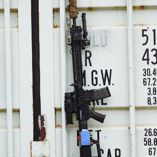 RIFLE WITH THERMAL SCOPE LEANING AGAINST SHIPPING CONTAINER